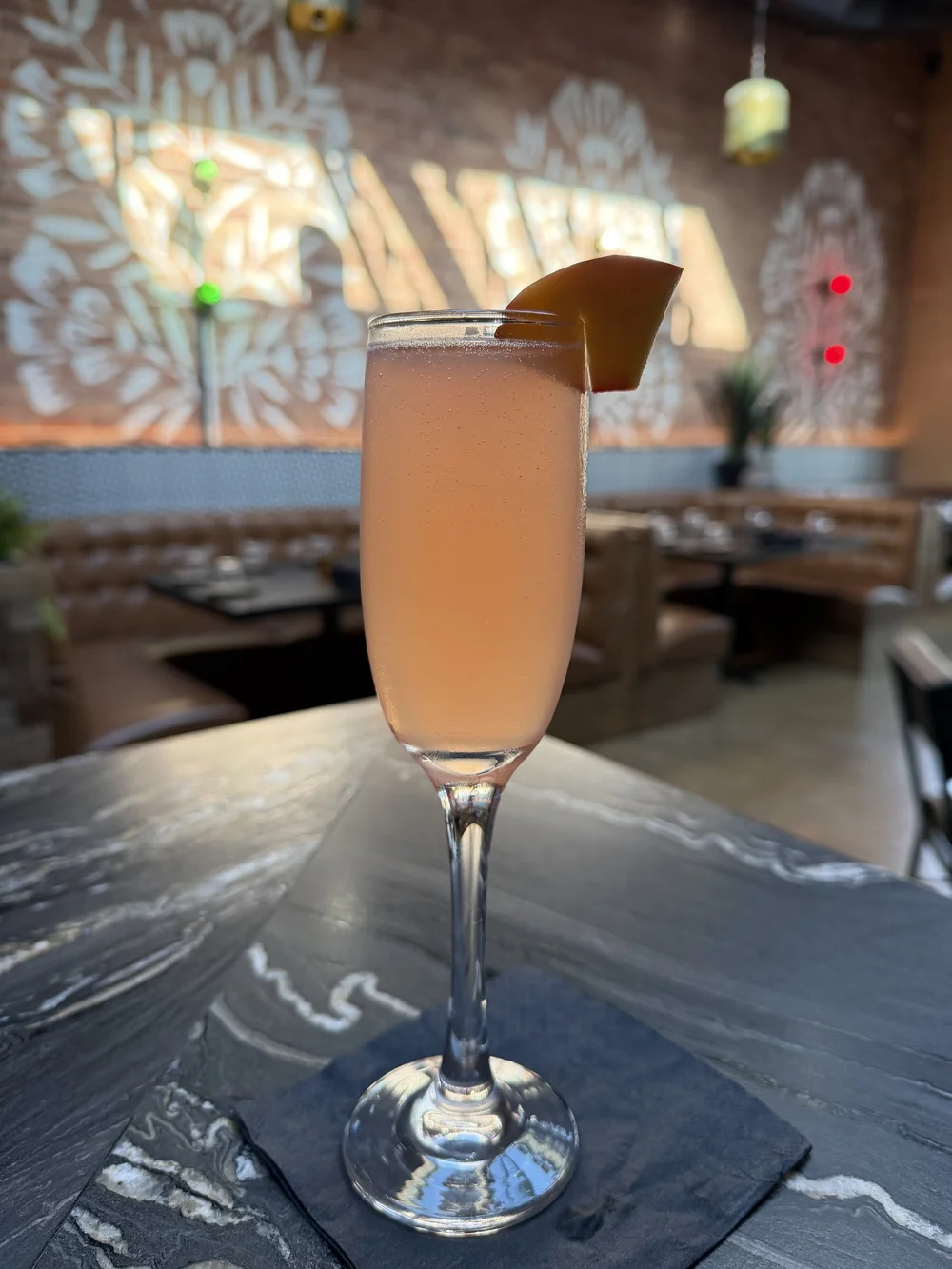 Aperol Jamaica Spritz catching the light of the stenciled brick wall