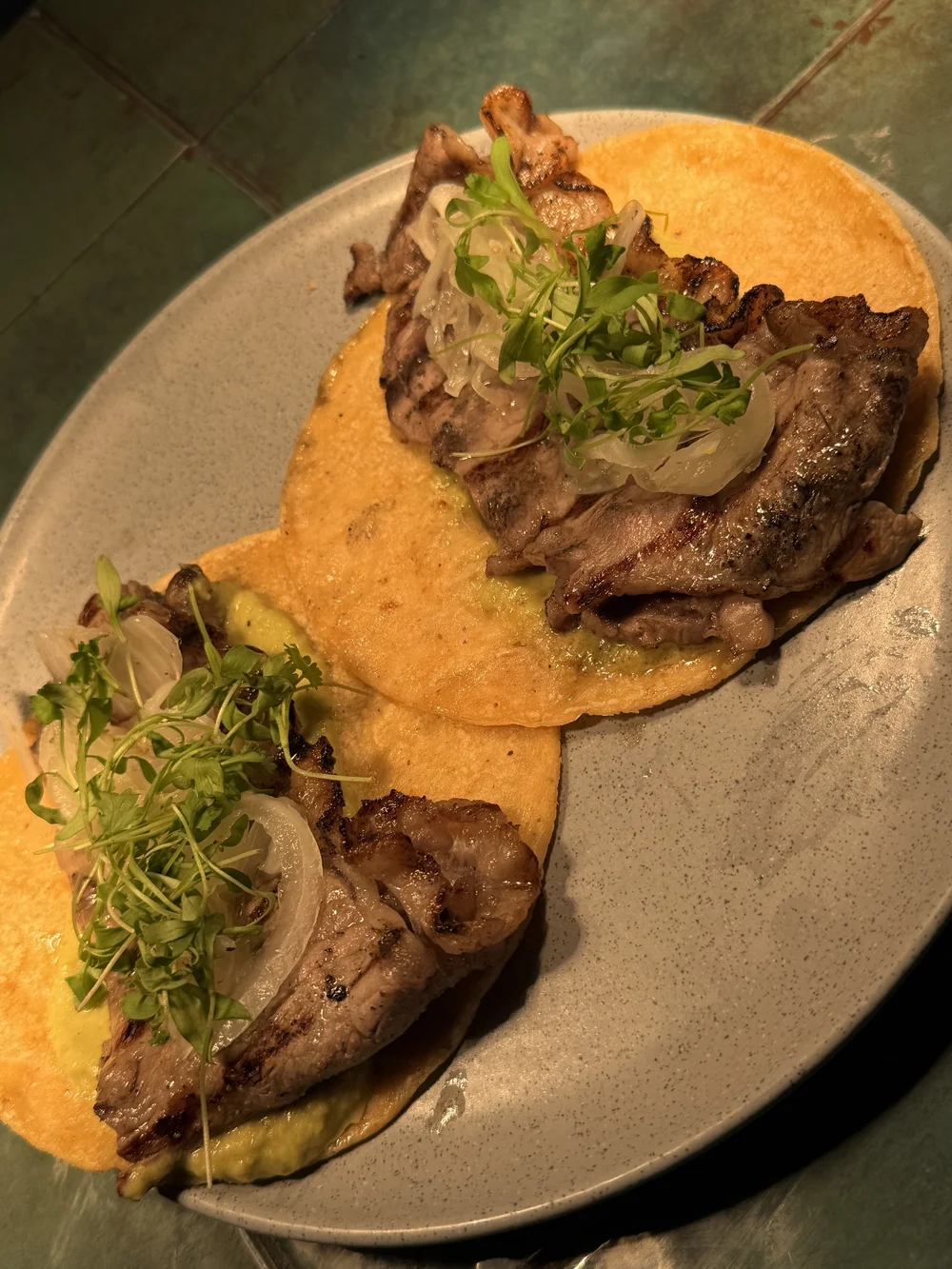 Two steak tacos on handmade tortillas with shaved onion and microgreens