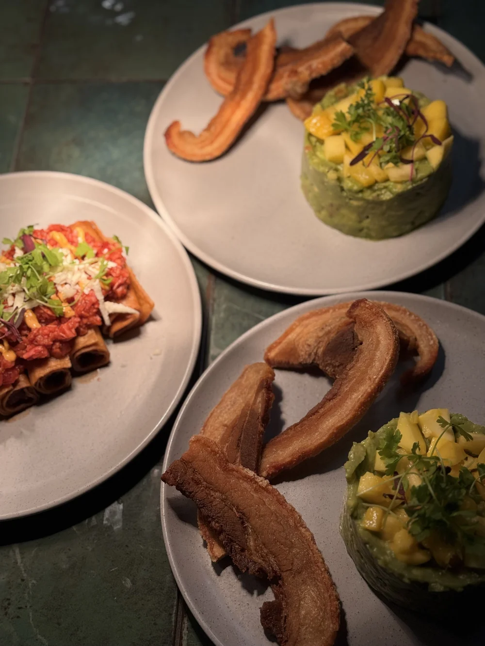 Flautas, guacamole with mango, and crispy pork belly on the green tile table