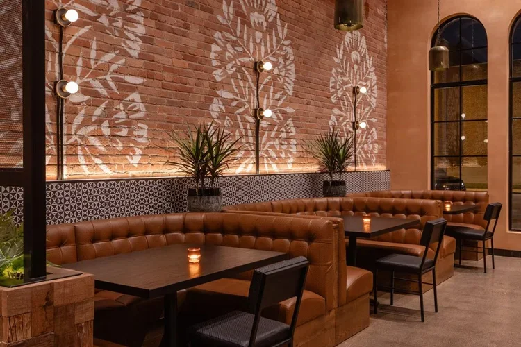 Brick wall with white botanical murals over tufted leather banquettes