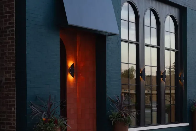 The deep-teal facade at dusk, arched steel windows and a glowing terracotta entry