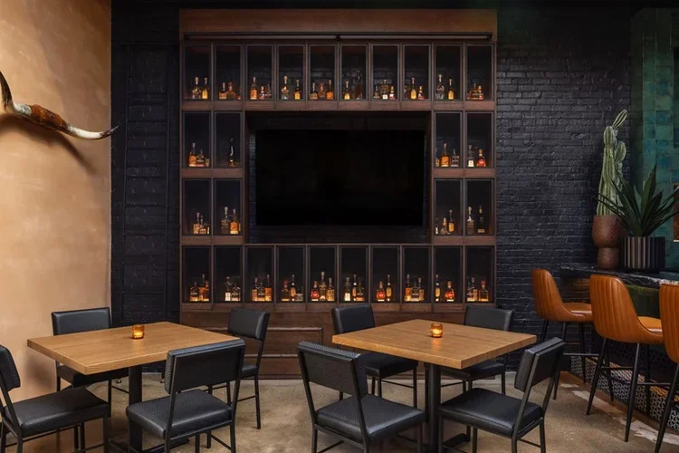 The members' liquor-cage wall, bottles glowing behind glass on black brick