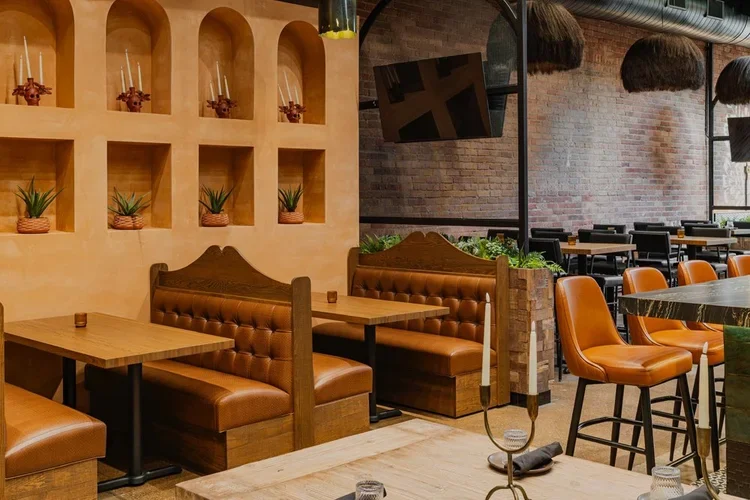 Arched adobe niches holding candles and small plants above cognac leather booths