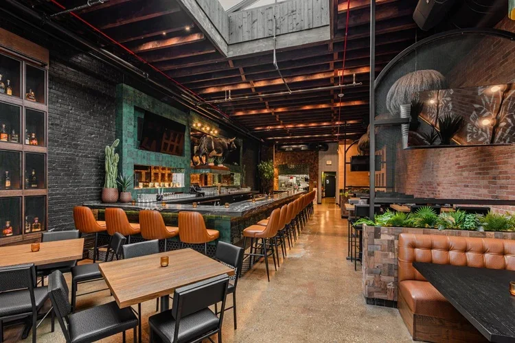 The full dining room under a skylight and timber ceiling, banquettes wrapped in greenery